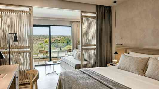 Hotellrum med en dubbelsäng, sittgrupp och en balkong med utsikt över natur. (AI-genererad text)