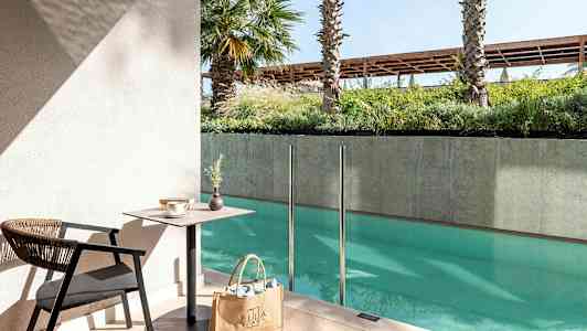 En sittgrupp med bord och stol vid en pool med glasräcke. (AI-genererad text)