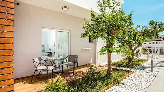 En terrass med trätrall och två stolar kring ett bord, omgiven av växter och ett citrusträd. (AI-genererad text)