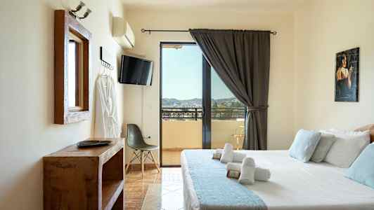 Ett hotellrum med en säng, tv, stol och utsikt över en balkong. (AI-genererad text)