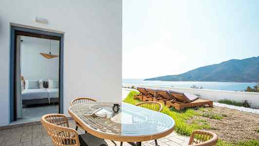 Utemöbler med bord och stolar framför en rummöppning och solstolar i en trädgård med utsikt mot havet. (AI-genererad text)