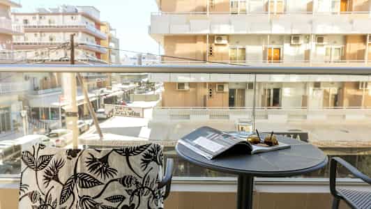 En balkong med utsikt mot flerfamiljshus. På bordet ligger glas, solglasögon och en tidning. (AI-genererad text)