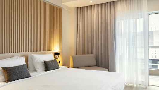 Sovrum med en dubbelbädd, träpanel på väggen och stora fönster med ljusa gardiner. (AI-genererad text)