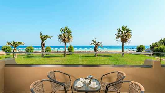 Utsikt från en terrass mot en strand med solstolar och palmer, med bord och stolar i förgrunden. (AI-genererad text)