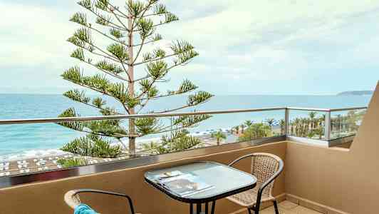 En balkong med utsikt över havet och stranden, med ett bord och stolar. (AI-genererad text)