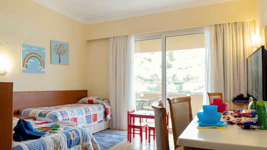 Ett hotellrum med två enkelsängar och ett bord med stolar nära en balkong. (AI-genererad text)