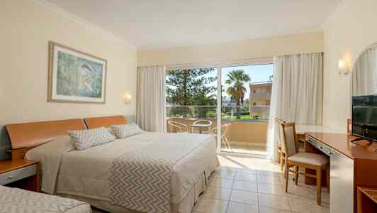 Ett hotellrum med bäddad säng, skrivbord och stolar bredvid en glasdörr som leder till en balkong. (AI-genererad text)