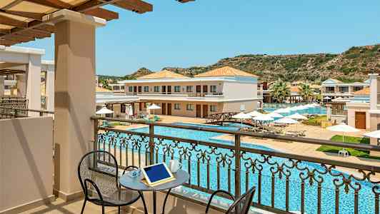 Vy från en balkong mot en pool och hotellbyggnader med solstolar och parasoller. (AI-genererad text)