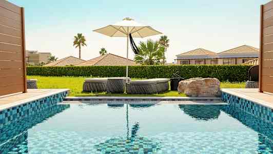 En swimmingpool med solstolar och ett parasoll i bakgrunden. (AI-genererad text)