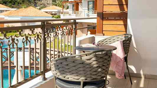 En balkong med två sittplatser, ett litet bord, och en fin utsikt över en swimmingpool och byggnader. (AI-genererad text)