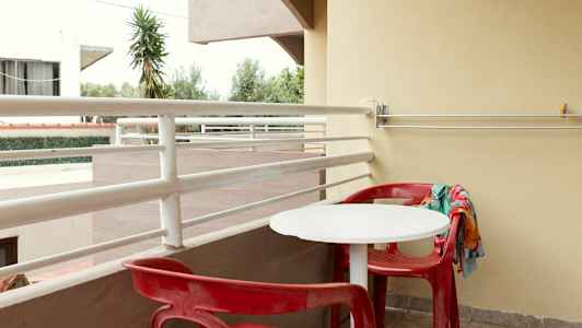 En balkong med röda stolar och ett vitt bord. (AI-genererad text)