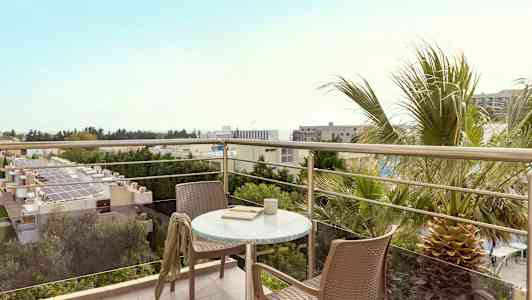 Utsikt från en balkong med bord och två stolar, omgivet av träd och byggnader. (AI-genererad text)