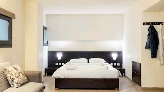 Ett hotellrum med en dubbelsäng, en soffa och en klädhängare. (AI-genererad text)