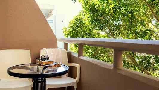 Balkong med bord och stolar, böcker och ett par solglasögon, med grönska i bakgrunden. (AI-genererad text)