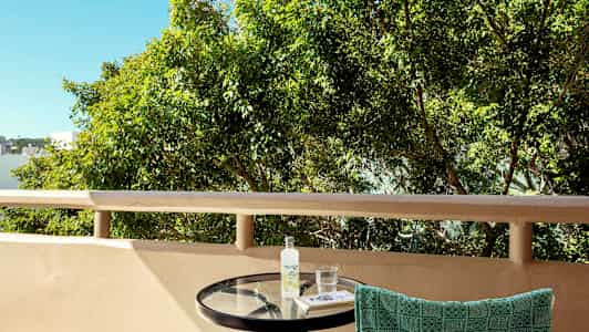 Bild av en balkong med ett runt bord, en handduk hängande på stolsryggen, samt träd i bakgrunden. (AI-genererad text)