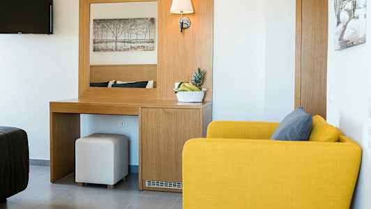 Ett hotellrum med en gul fåtölj, ett skrivbord med spegel och en skål med frukt. (AI-genererad text)