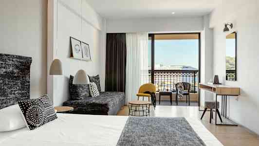 Modernt hotellrum med säng, soffa och sittgrupp samt utsikt mot balkong och omgivning. (AI-genererad text)