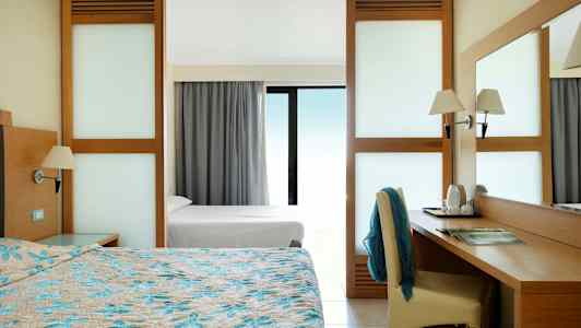 Hotellrum med dubbelsäng, skrivbord och utsikt genom ett glasat fönster. (AI-genererad text)