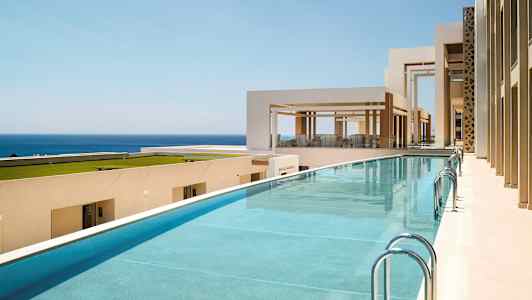 Bild av en pool vid ett modernt, ljust byggnadskomplex med utsikt över havet. (AI-genererad text)