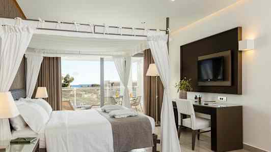 Ett elegant hotellrum med en himmelssäng, skrivbord och utsikt mot havet från en balkong. (AI-genererad text)