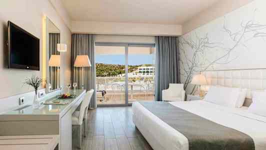 Ett modernt hotellrum med en stor säng, arbetsbord, TV och balkong med utsikt. (AI-genererad text)