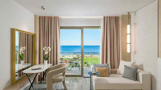 En moderne hotellsvit med soffa, bord, stolar och utsikt över havet genom ett stort fönster. (AI-genererad text)