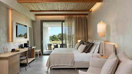 Ett modernt hotellrum med en dubbelsäng, en sittgrupp och ett skrivbord. Tyg för in dagsljus från altanutgången. (AI-genererad text)