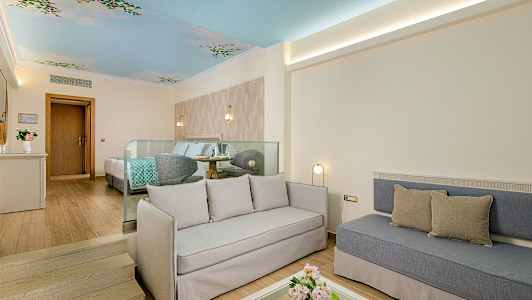 Ett ljust hotellrum med sittgrupp, säng och dekorerat tak. (AI-genererad text)