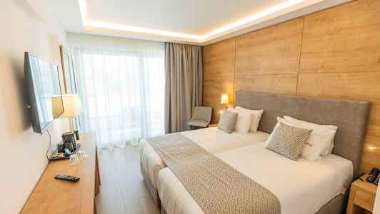 Ett modernt hotellrum med två enkelsängar, väggmonterad TV, träpanelvägg och stora fönster. (AI-genererad text)