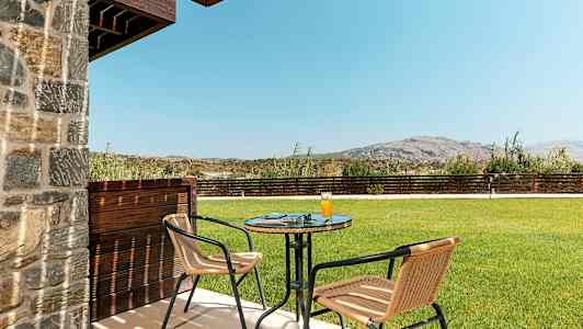 Uteplats med bord och två stolar, gräsmatta och berg i bakgrunden. (AI-genererad text)