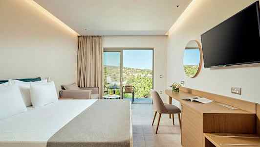 Ett modernt hotellrum med en dubbelsäng, skrivbord och stol samt en balkong med utsikt över grönskande terräng. (AI-genererad text)