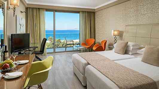 Hotellrum med sängar, sittmöbler och utsikt över havet. (AI-genererad text)