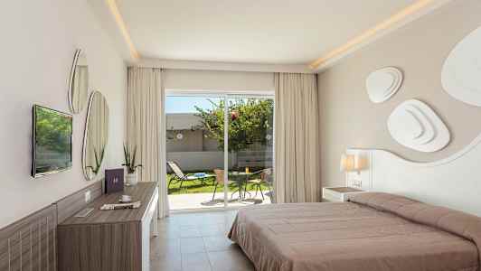 Ett hotellrum med en dubbelsäng, skrivbord, och en utsikt mot en privat trädgårdsområde med möbler genom glasdörrar. (AI-genererad text)