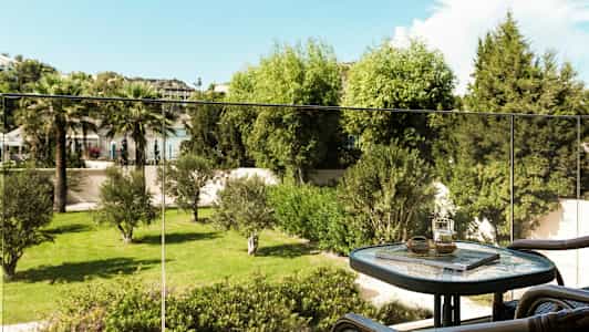 En balkong med ett bord och stolar samt utsikt mot en grön trädgård. (AI-genererad text)