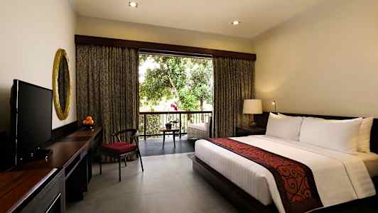 En hotellrum med en stor säng, ett skrivbord med en guldspegel och en TV. Fönstret öppnar upp mot en balkong med utsikt över gröna träd. (AI-genererad text)