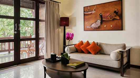 Ett vardagsrum med en soffa, bord och dekorationer framför stora glasdörrar med utsikt mot en veranda. (AI-genererad text)