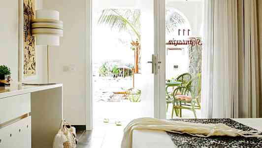 Ett hotellrum med öppet glasdörr till en terrass med gröna stolar. (AI-genererad text)