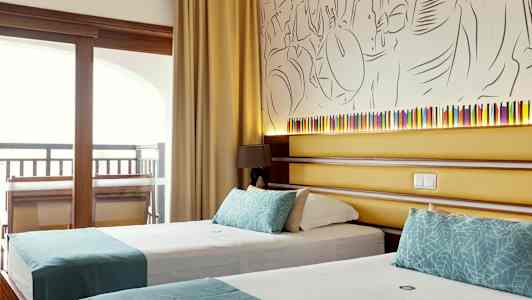 Ett hotellrum som visar två enkelsängar med turkosa dekorationer, bakom sängarna finns en vägg med konstnärlig dekoration och en liten lampett. (AI-genererad text)