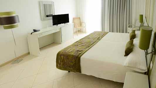 Hotellrum med en dubbelsäng, skrivbord med spegel och TV, samt en lamparmatur. (AI-genererad text)