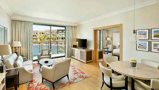 Ett hotellrum med ett vardagsrum, matbord och en balkong som vetter mot en utomhuspool. (AI-genererad text)