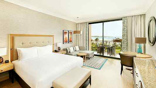 Ett hotellrum med en stor säng, sittgrupp, skrivbord och en uteplats som vetter mot havet. (AI-genererad text)