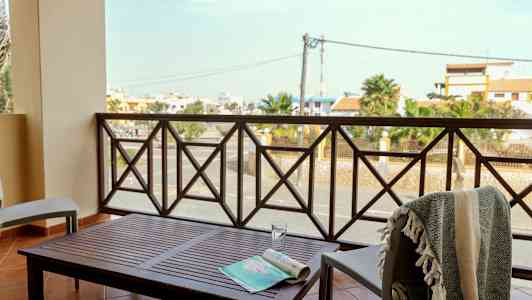 En balkong med bord och stolar, med utsikt över en gata och byggnader. (AI-genererad text)