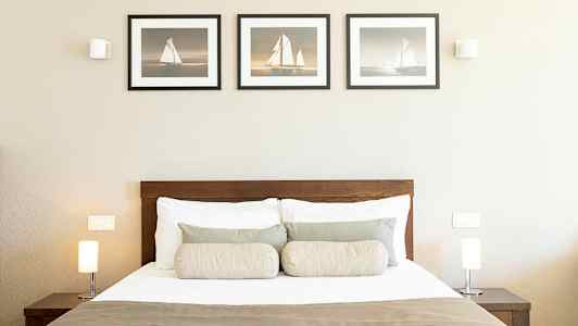 Ett sovrum med en säng, två lampor på nattduksbord och tre tavlor på väggen. (AI-genererad text)