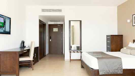 Ett modernt hotellrum med säng, skrivbord, TV och spegel. (AI-genererad text)