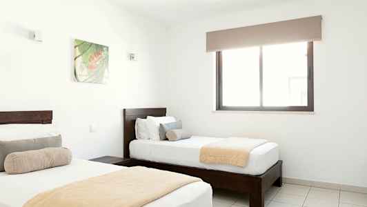 Två enkelsängar i ett ljust sovrum med ett fönster och en väggdekoration. (AI-genererad text)