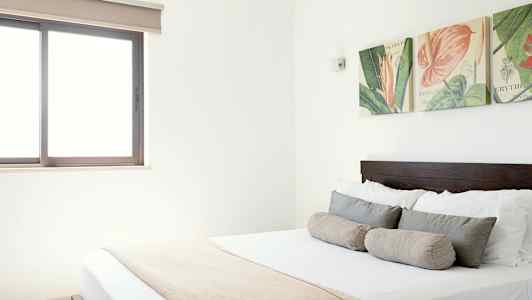 Bild av ett ljust sovrum med en dubbelsäng, dekorativa kuddar och väggdekorationer ovanför sängen. (AI-genererad text)