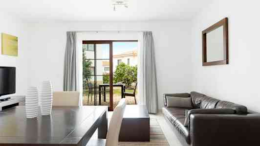 En modern inredd vardagsrum med matsalsbord, soffa och bord samt stora fönster mot en utomhusterrass. (AI-genererad text)