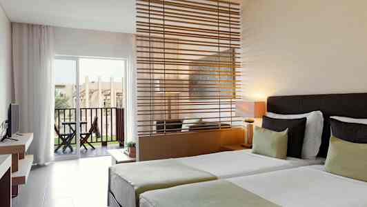 Hotellrum med två enkelsängar, en sittplats med en avdelare, och en terrass med utsikt. (AI-genererad text)