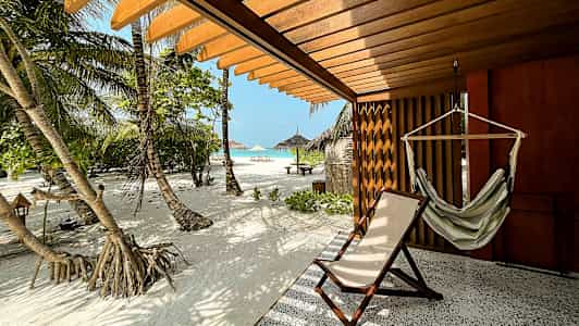 Terrass med hängmatta och solstol, utsikt över sandstrand och palmer. (AI-genererad text)