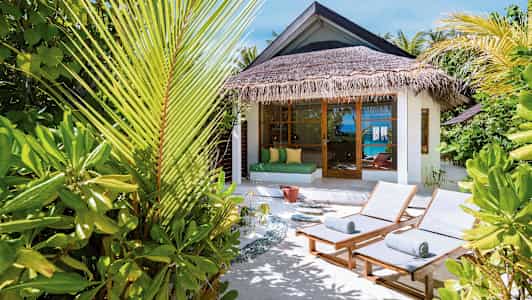 Solstolar och tropiska växter vid en bungalow med havsutsikt. (AI-genererad text)